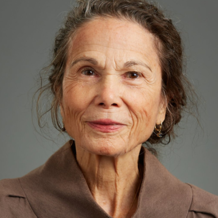 author Julia Alvarez, wearing a tan blouse and hair pulled back, looks at the camera for a portrait