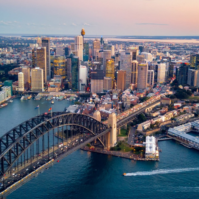 An aerial view of the Sydney with the Sydney skyline, Harbor Bridge, and Opera House in view during sunset