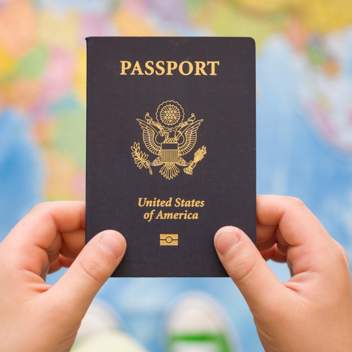 A boy holds a US passport against a globe themed carpet