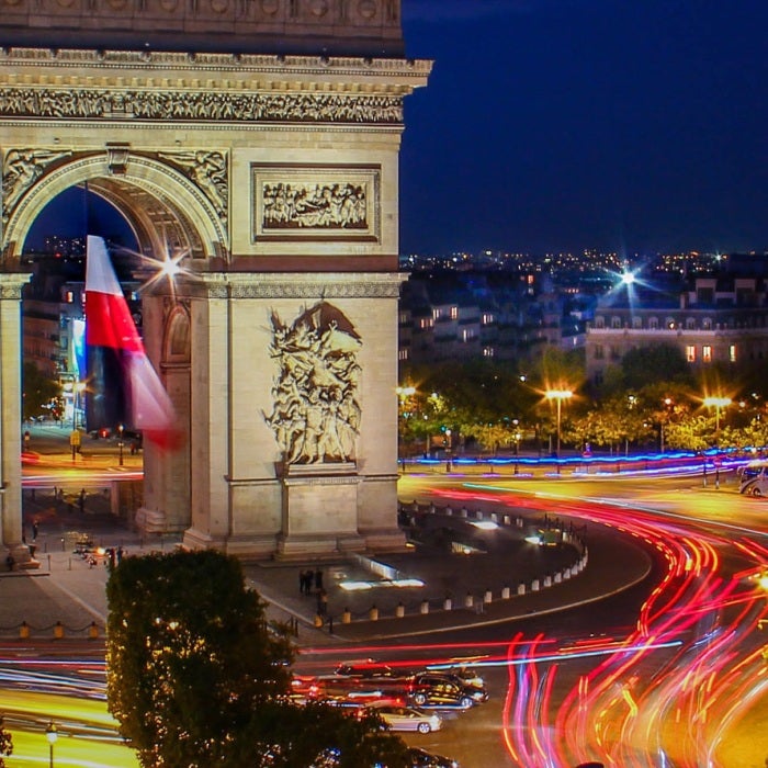 The famous Arc de Triomphe arch illuminated by motorists at night in Paris, France