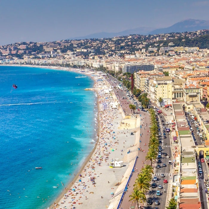 Nice, France, part of the French Riviera in southern France, is situated along the turquoise Mediterranean sea, is backdropped by distant mountains on a beautiful blue sky day.