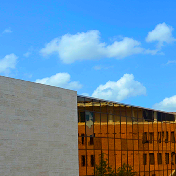 An image of a triangular building on UT campus with blue sky in the background and the Tower to the left side