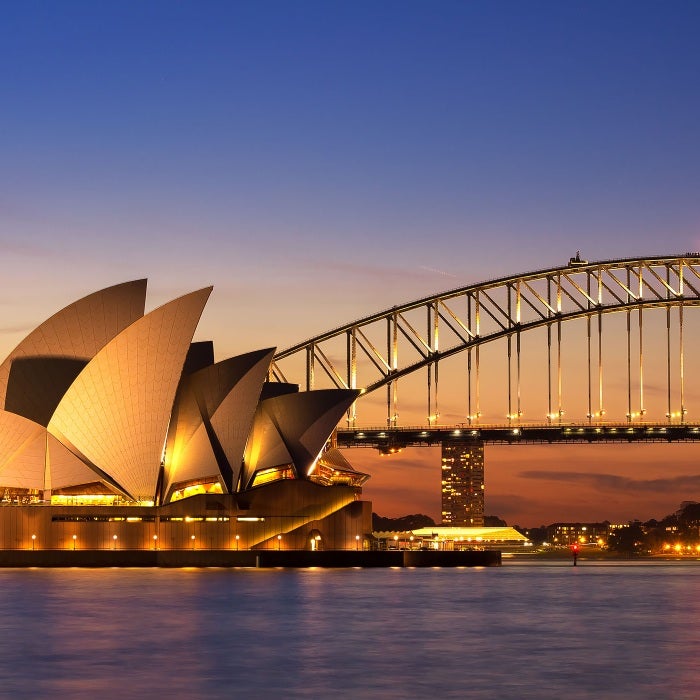 The beautiful Sydney Opera house during a colorful sunset at twilight time with illumination on the bridge behind it