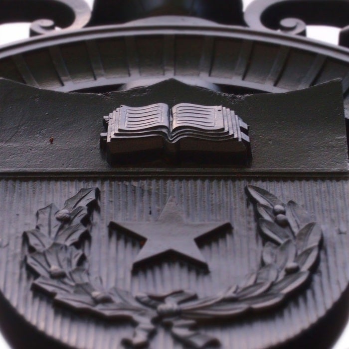 A closeup of the Univesity seal is displayed on a gate.