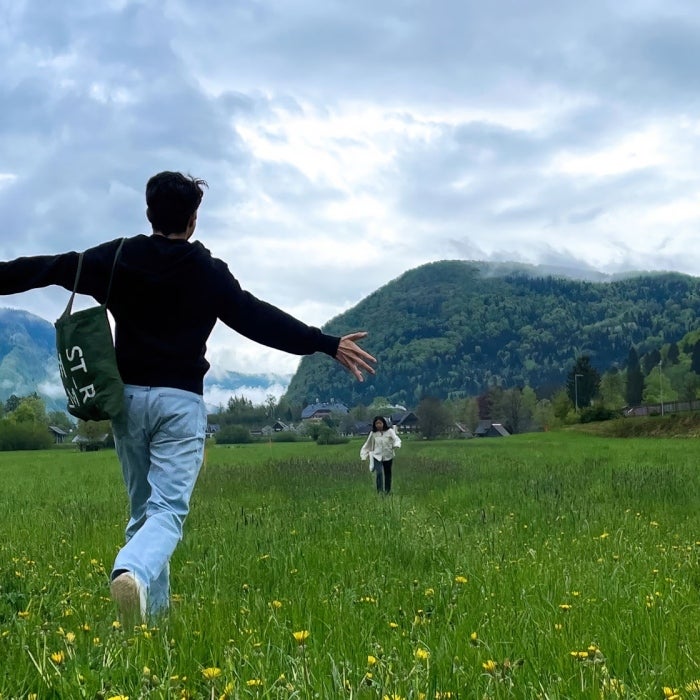 a young man runs through a field with mountains in the distance to his family