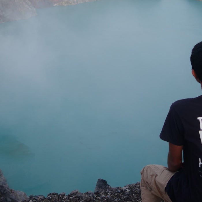A male UT student wearing a take the world by the horns shirt stares down at a large turquoise water filled crater