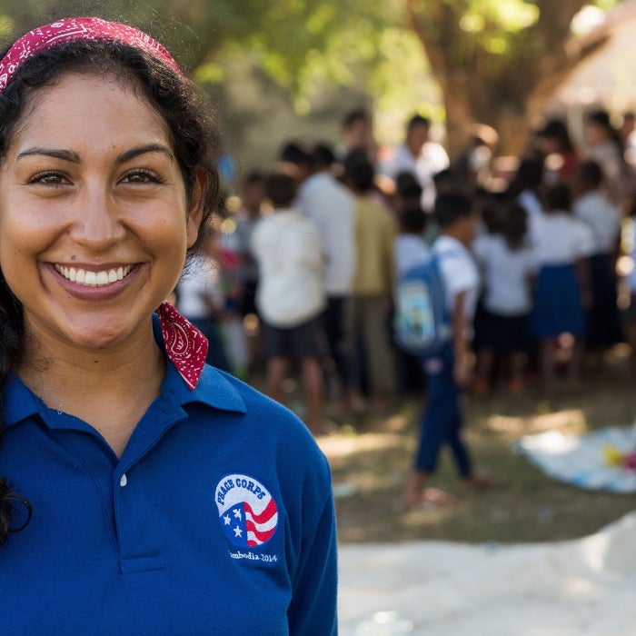 A female Peace Corps Volunteer in a Peace Corps shirt poses, smiling in front of members of her community during service work