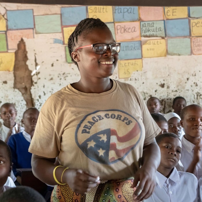 A smiling female peace corps volunteer aids with teaching in an African school