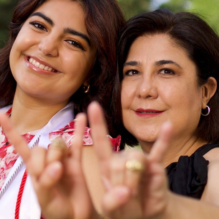A graduating student and her mother smile and while displaying the hook'em sign
