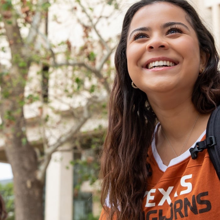 A sitting student smiles while wearing a Texas Longhorns shirt on campus