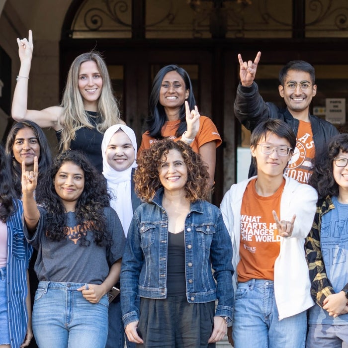 Smiling ISSS students pose for a group photo on the main building stairs while displaying the hook'em sign