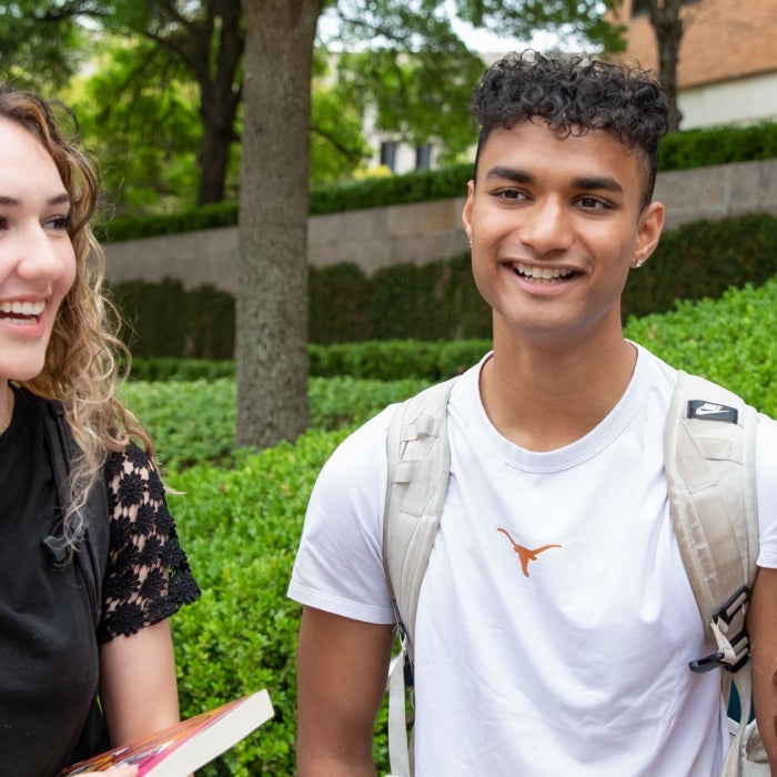 Smiling students wearing UT branded clothing chat on campus