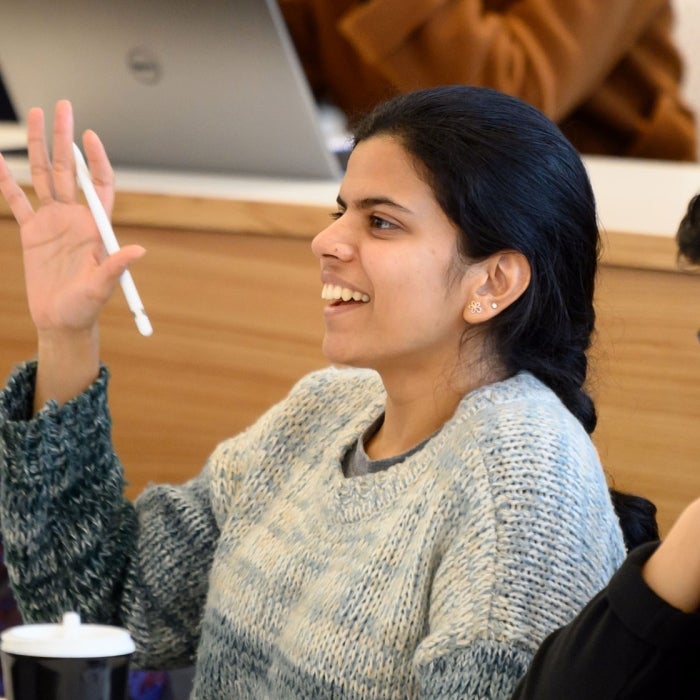 A smiling female student raises her hand in class