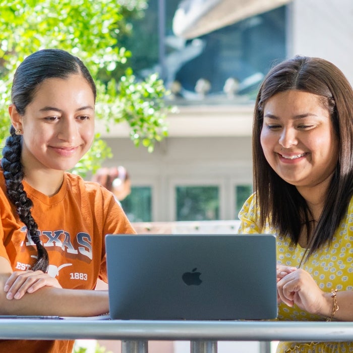 two female students look at courses on a laptop at a table outside on the UT campus