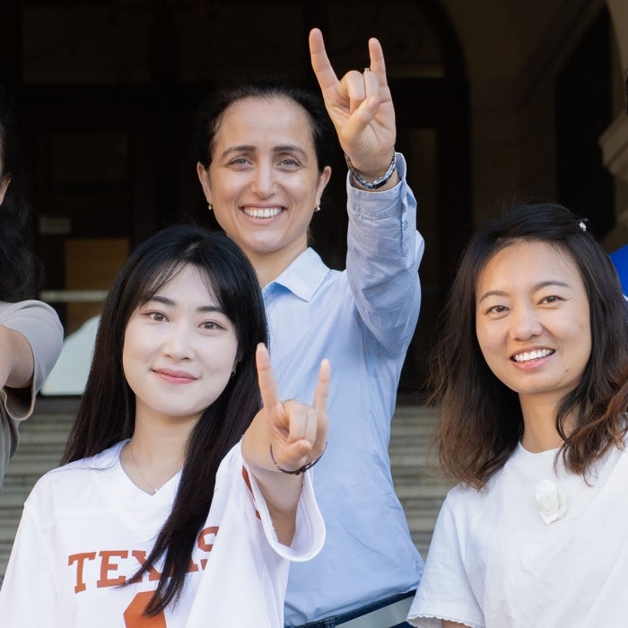 A group of smiling longhorns show the Longhorn hook'em sign in a group photo on the main building entryway stairs