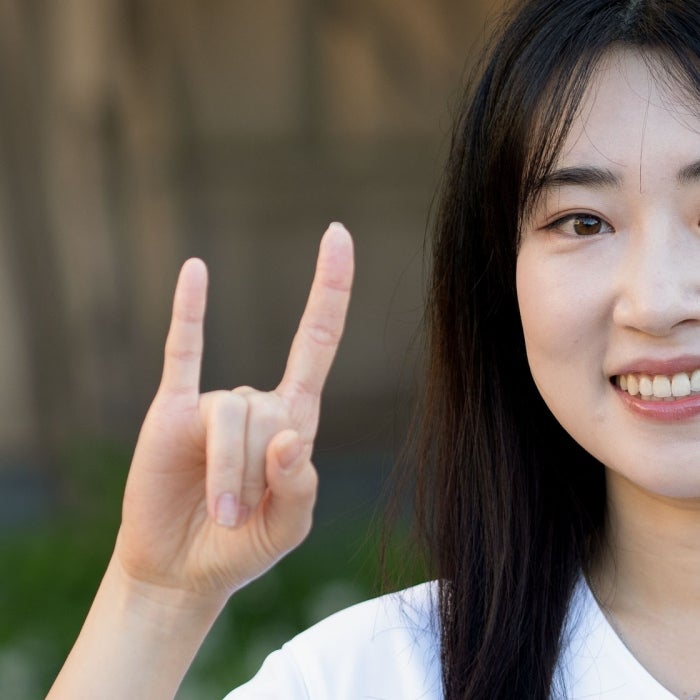 A female asian student smiles while showing her Longhorn pride with the hook'em sign