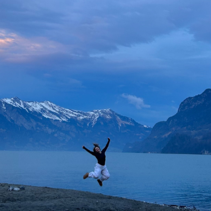 Student jumping up in front of alpine lake with snowy mountain backdrop