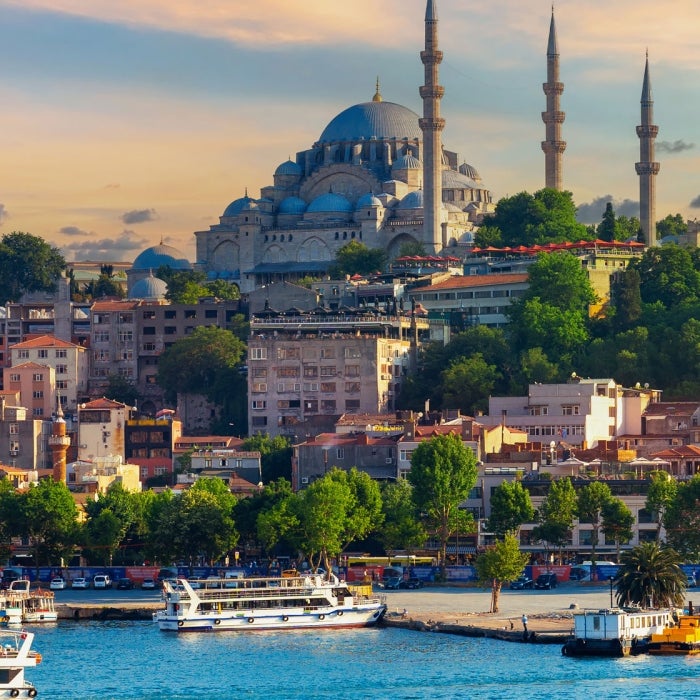 Tourist sightseeing ships cruise the aquarmarine waters that touch the city of Istanbul, Turkey with the impressive Suleymaniye Mosque in the background