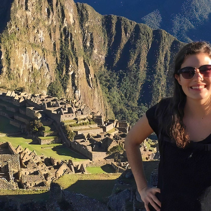 A female student shows the hook'em sign high up in the famous ruins of Machu Picchu in Peru on a clear blue sky day