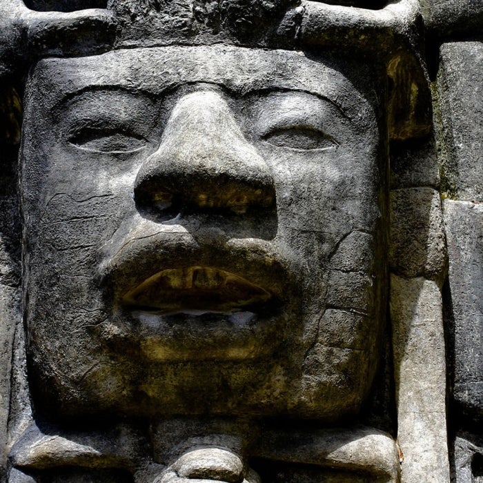 A female student abroad stares at a large ancient stone carving of a face adorned with other geometric motifs