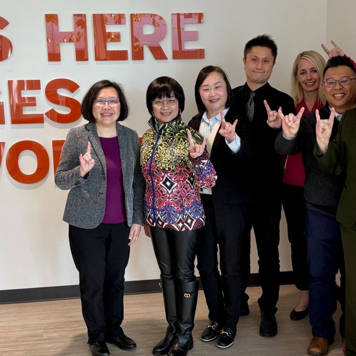 A delegration group smiles for a photo in the renovated Texas Global lobby - what starts here changes the world slogan is on the wall