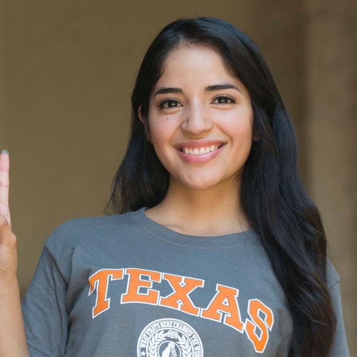 A female latin student smiles while showing the hook'em sign