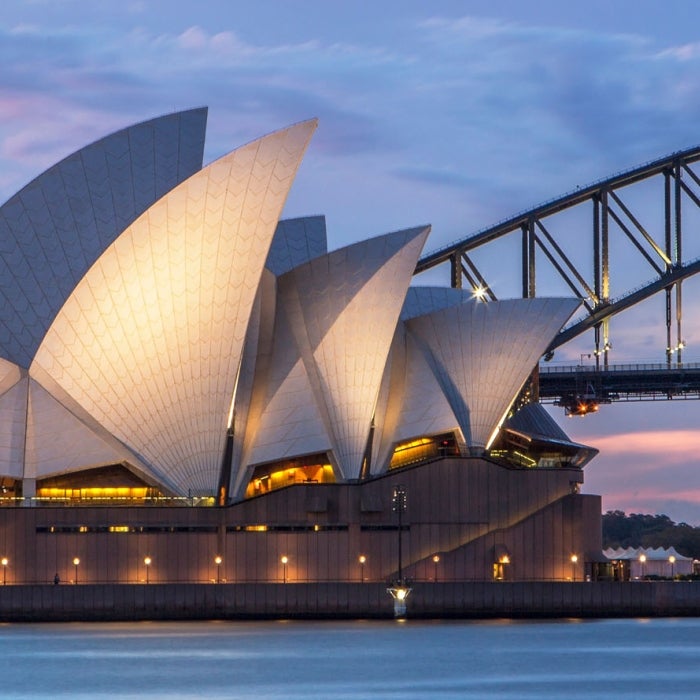 The illuminated Sydney Opera House and Harbor Bridge backdropped by an evening blue and pink sunset in Sydney, Australia