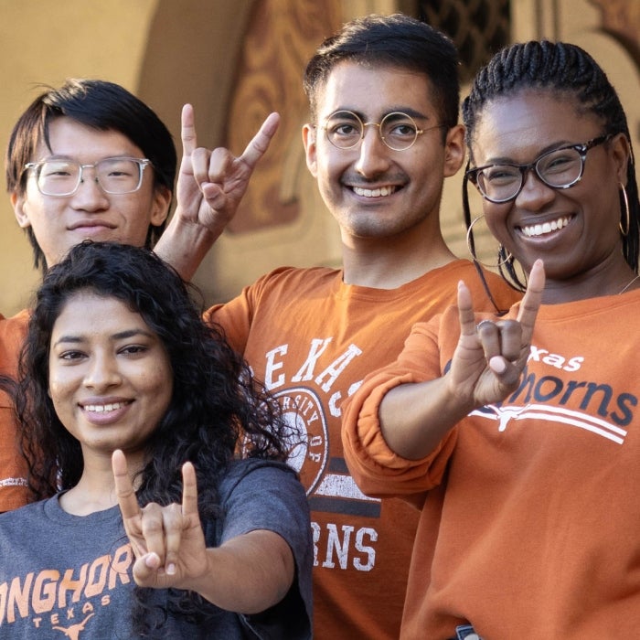 A diverse mix of smiling students in UT burnt orange shirts show off their Longhorn hook'em hand sings