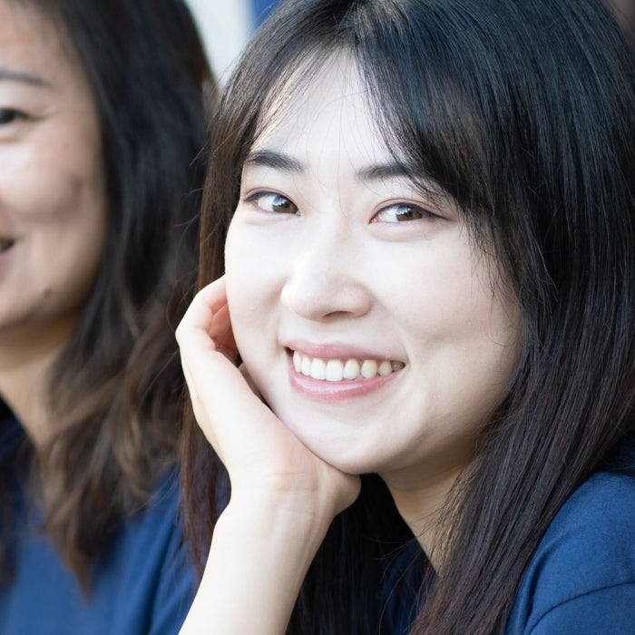 A young asian student smiles with her hand on her face, other students smile in the background