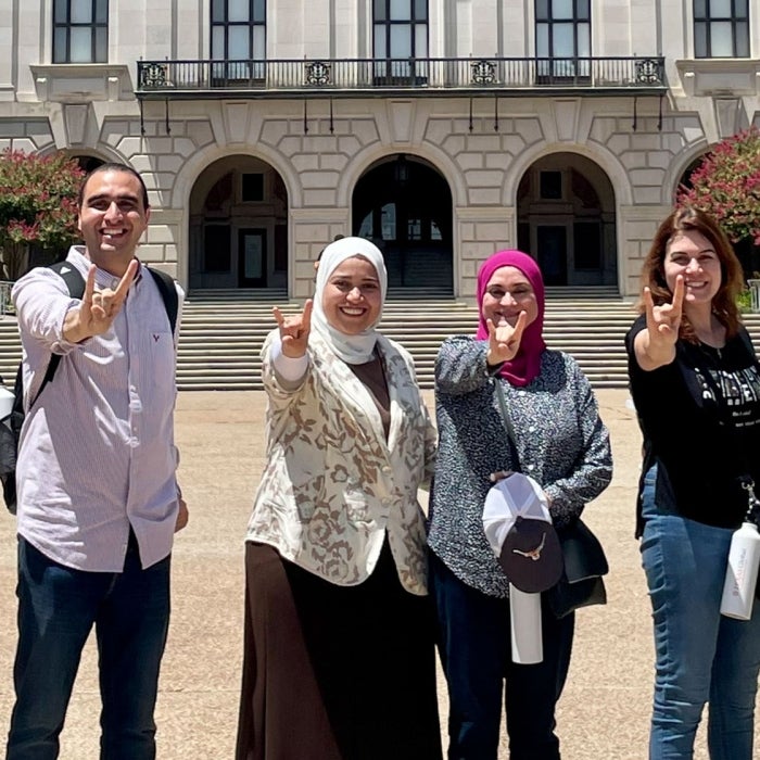 A group of Fulbright students from Egypt smile while displaying the hook'em sign in front of the UT Tower
