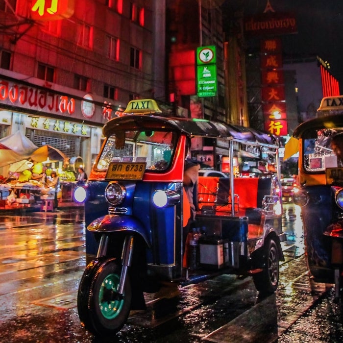 Looking down a wet and neon lit street in Asia with electric richshaws in the foreground