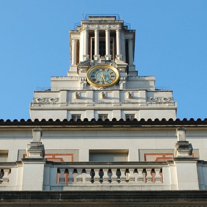 The UT tower stands tall against a blue sky with the main building facade in front of it