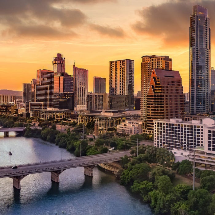 An aerial view of Lady Bird Lake and downtown Austin during a beautiful orange sunset looking north towards the skyline. You can see the Congress, South First, and Lamar Bridges.