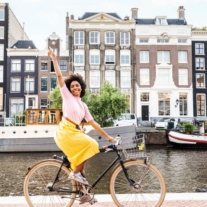 Smiling woman riding bicycle in urban street along a canal in Amsterdam, Netherlands