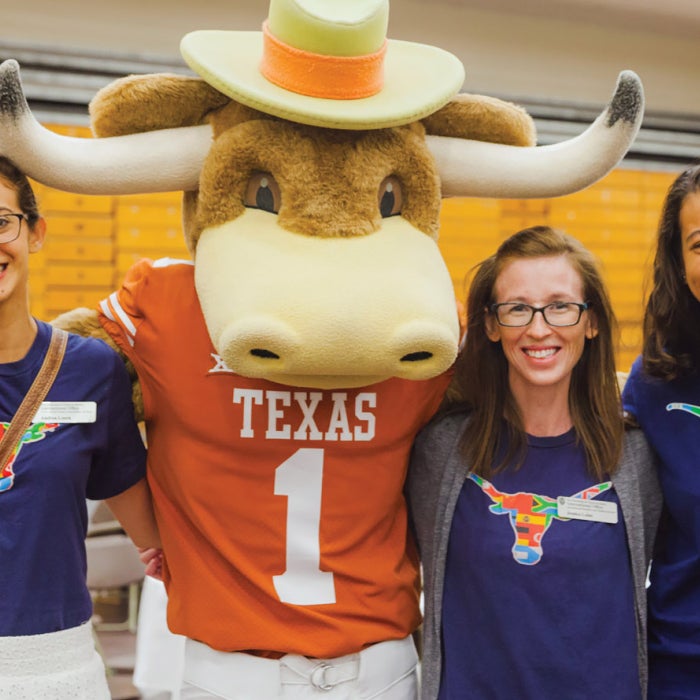 female longhorns in texas global shirts smile and pose with the UT longhorn mascot