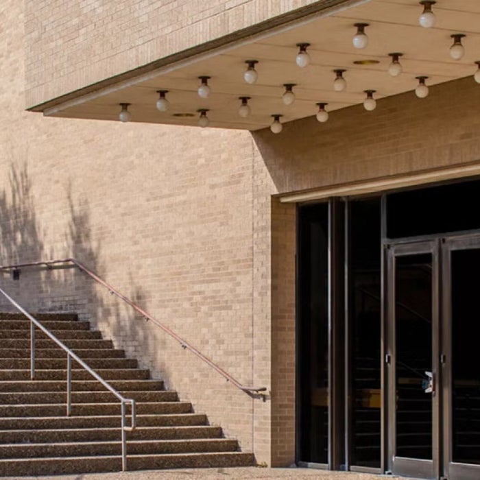 Building entrance with multiple glass doors and a large overhead marquee. Adjacent stairs with metal railing lead to an upper walkway.