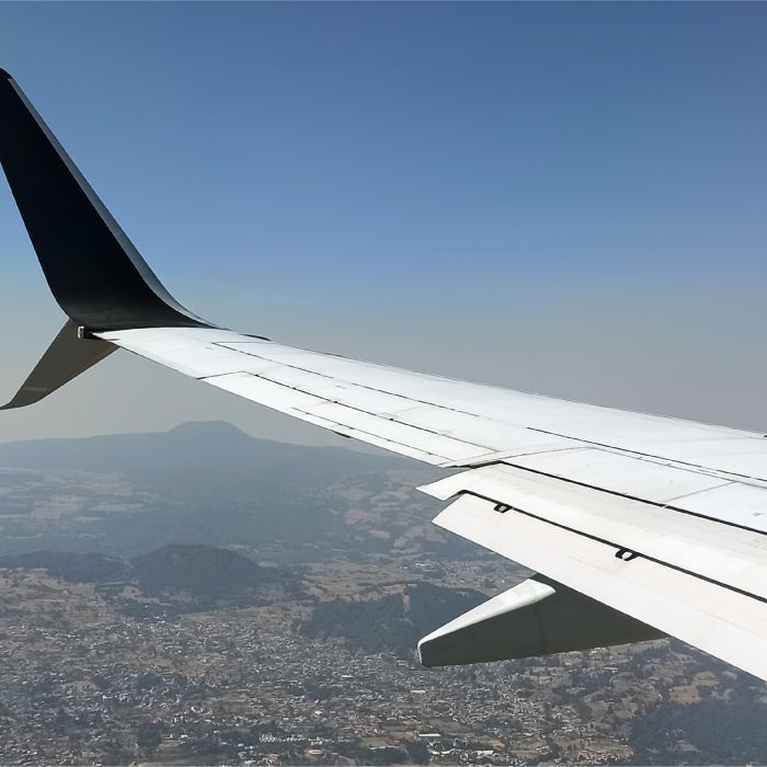 An airplane wing over an aerial landscape of a mountainous city
