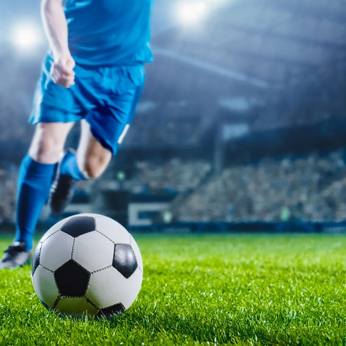 Soccer player runs towards the ball on grass field of a stadium, backdropped by lights and a seats full of cheering fans