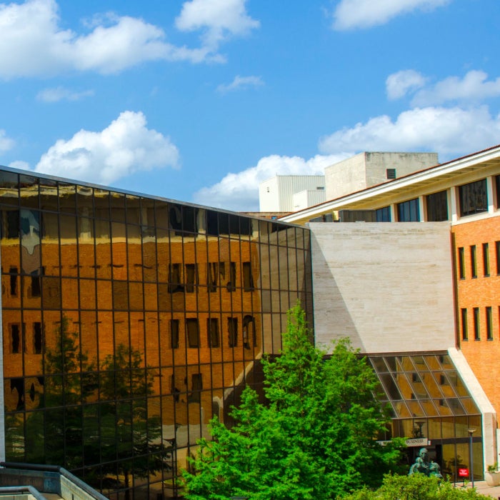 Graduate School of Business building at McCombs against a blue sky with puffy clouds and the UT Tower standing high in the background