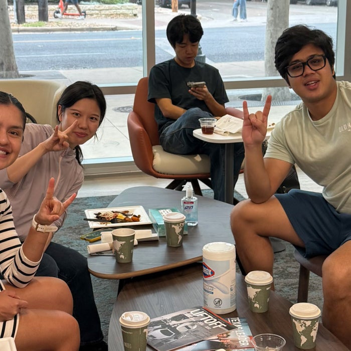 International students enjoy breakfast and fellowship in Texas Global lounge. They smile for a photo and display the hook'em sign.