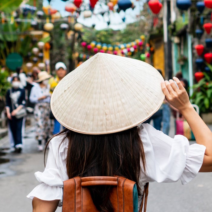 Carefree tourist woman wearing  a traditional Vietnamese hat enjoy sightseeing in the colorful Hoi An old town, Vietnam