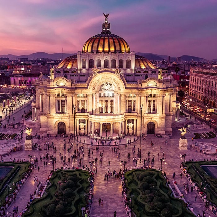 A stunning of view of the Palace of Fine Arts illuminated against a backdrop of a beautiful pink, purple, and orange sunset in the evening in Mexico City, Mexico