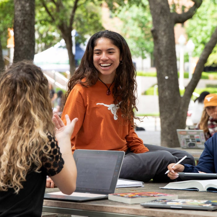 a mix of students talking together and smiling outside on the UT Austin campus