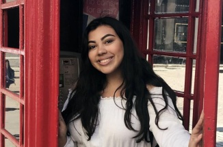 UT Student Briana Rodriguez smiles and poses in a phone booth