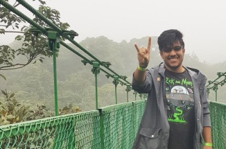 UT student Feliciano poses with hook'em horns hand sign in front of a bridge in Costa Rica