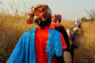 Photo of African women dressed in traditional wardrobe, walking through a field 
