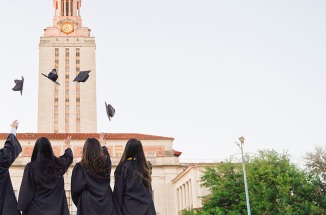 four UT grads throw up their caps in front of the tower
