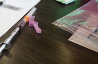 A pen and syringe lie on top of medical forms and papers on a desk