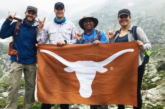 Four people standing in a valley in Slovakia hold up a University of Texas "Bevo" flag