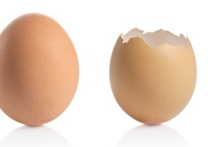 Two eggs lie beside each other on a white background, one cracked and the other uncracked.